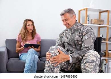 Shocked Wife Looking At Injured Soldier Sitting On Wheelchair Suffering From Knee Pain At Home