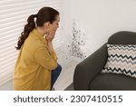 Shocked woman looking at affected with mold walls in room