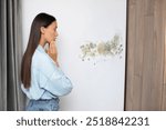 Shocked woman looking at affected with mold wall in room, thinking what to do and which service call