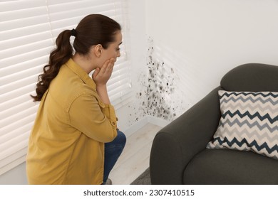 Shocked woman looking at affected with mold walls in room