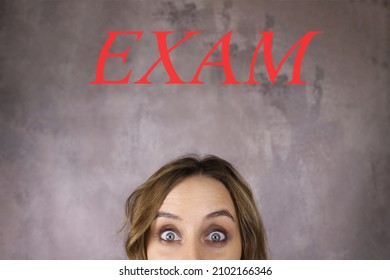 Shocked Woman Looks At The Word Exam On A Gray Background