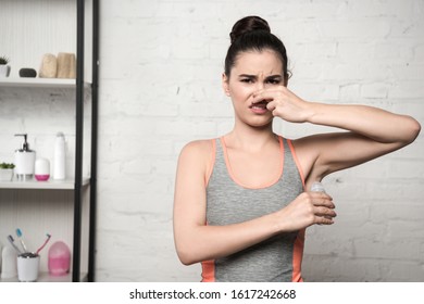 Shocked Woman Plugging Nose With Hand While Applying Deodorant On Underarm