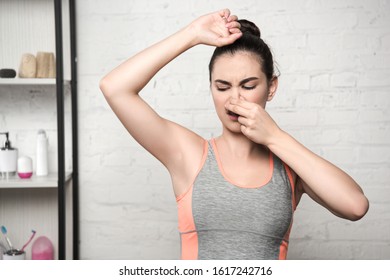 Shocked Woman Plugging Nose With Hand While Looking At Underarm