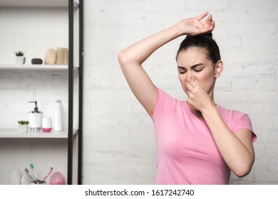 Shocked Woman Plugging Nose With Hand While Looking At Underarm