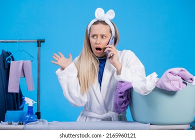 A Shocked Woman In A Robe And Headband Is Talking On The Phone Is Upset Surprised To Hear The News. Interruption Of Household Chores Ironing.