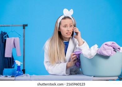 A Shocked Woman In A Robe And Headband Is Talking On The Phone Is Upset Surprised To Hear The News. Interruption Of Household Chores Ironing.