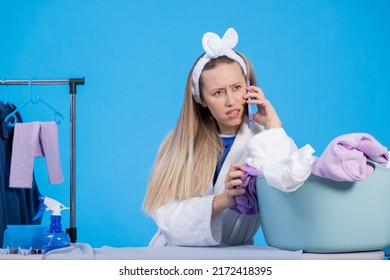 A Shocked Woman In A Robe And Headband Is Talking On The Phone Is Upset Surprised To Hear The News. Interruption Of Household Chores Ironing.