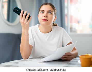 Shocked Woman Talking On Phone With Bank Customer Service While Checking Documents At Home