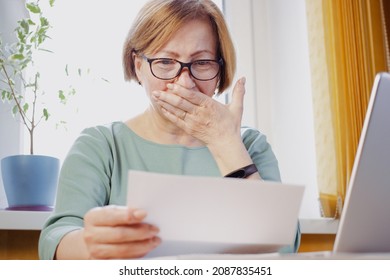 Shocked Worried Mature Woman Reading Paper Document Or Postal Letter Feeling Frustrated By Unexpected News Sitting At Home Indoor. Received Bank Account Balance Or Bad Notice, Fine, Bankruptcy