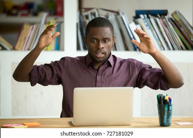 Shocked Young African American Office Worker Looking At Laptop Screen Throwing Arms In The Air. Horrified Small Business Owner Sees App Error, Lost Documents Because Of Unexpected Bad Computer Crash. 