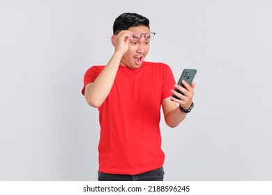 Shocked Young Asian Man Looking At Mobile Phone Screen Reacting To Online News With Opened Mouth Isolated Over White Background