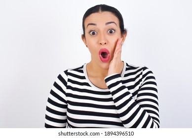 Shocked Young beautiful woman wearing stripped t-shirt against white background looks with great surprisment being very stunned, astonished with unexpected news, Facial expressions concept.