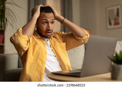 Shocked Young Black Guy Looking At Laptop Screen, Grabbing His Head In Terror, Making Mistake, Missing Project Deadline At Home. Millennail African American Male Having Remote Work Stress