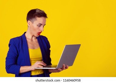 Shocked Young Business Woman Using Laptop Looking At Computer Screen Blown Away In Stupor Isolated On Yellow Background. Human Face Expression, Emotion, Feeling, Perception, Body Language, Reaction.