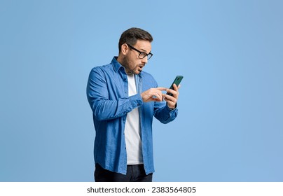 Shocked young businessman in eyeglasses reading bad news over mobile phone against blue background - Powered by Shutterstock