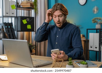 Shocked young businessman using smartphone typing browsing, loses becoming surprised sudden lottery results, bad news, fortune loss fail at home office desk workplace. Bearded freelancer worker man. - Powered by Shutterstock