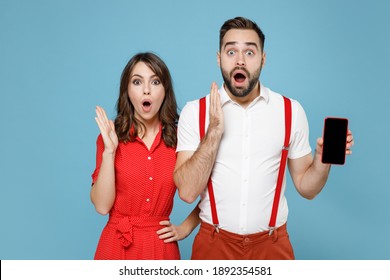 Shocked Young Couple Two Friends Man Woman Wearing White Red Clothes Hold Mobile Cell Phone With Blank Empty Screen Isolated On Blue Background Studio Portrait. St. Valentine's Day Holiday Concept