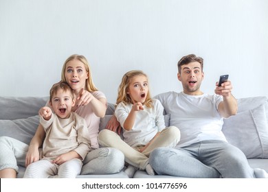 Shocked Young Family Watching Movie At Home And Pointing At Tv