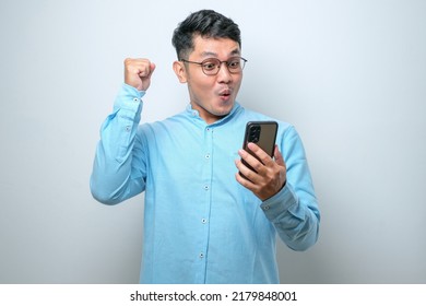 Shocked young good looking Asian man using smartphone to read good news online isolated on white studio background - Shutterstock ID 2179848001