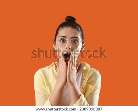 Shocked young gossip woman on orange background, closeup