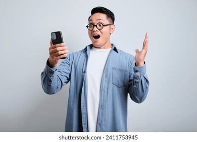 Shocked young handsome asian man wearing denim use eyeglasses is feel shocked and surprised when looking his phone, isolated on white background. - Powered by Shutterstock