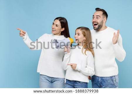 Shocked young parents mom dad with child kid daughter teen girl in sweaters screaming in megaphone pointing index fingers aside isolated on blue background. Family day parenthood childhood concept