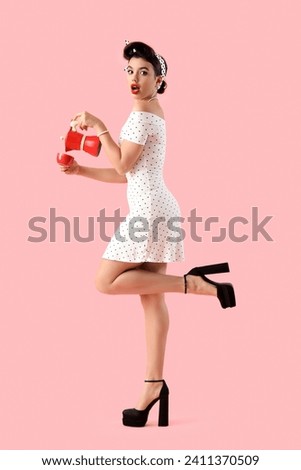 Shocked young pin-up woman with geyser coffee maker and cup on pink background