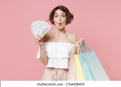 Shocked Young Woman Girl In Summer Clothes Isolated On Pink Wall Background. Shopping Discount Sale Concept. Mock Up Copy Space. Hold Package Bag With Purchases, Fan Of Cash Money In Dollar Banknotes