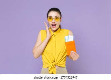 Shocked young woman girl in yellow shirt isolated on violet background. Passenger traveling abroad to travel on weekends getaway. Air flight journey concept. Hold passport, tickets, put hand on cheek - Shutterstock ID 1774326947