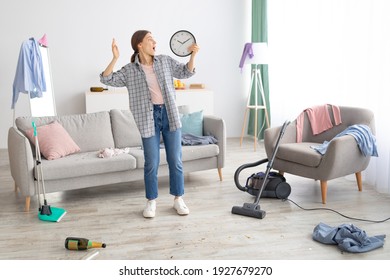 Shocked Young Woman Holding Clock, Feeling Terrified, Standing In Messy Room After Party, Being Late To Clean Apartment, Copy Space. Millennial Maid Not Meeting Cleanup Deadline