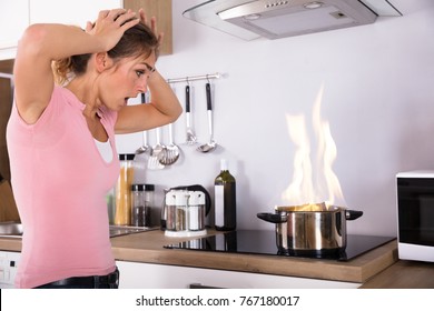 Shocked Young Woman Looking At Cooking Pot With Fire Near Modern Gas In Kitchen