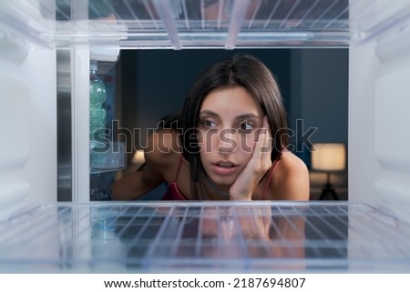 Shocked young woman looking in the empty fridge, she has no food at home, point of view shot from inside the fridge