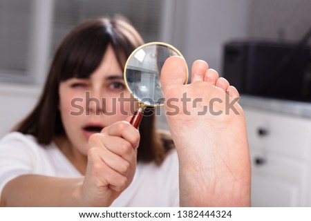 Shocked Young Woman Looking At Her Toe Nails With Magnifying Glass