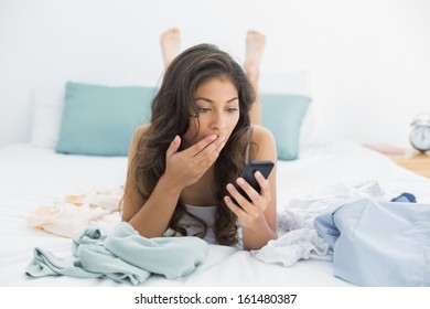 Shocked Young Woman Looking At Mobile Phone In Bed At Home