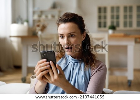 Shocked young woman looking at smartphone screen, feeling confused getting message with unbelievable news. Surprised millennial lady getting unexpected online lottery win notification at home.