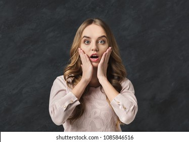 Shocked young woman with opened mouth in full disbelief. Surprised girl portrait, gray background. Omg, wtf, human emotions concept