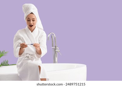 Shocked young woman with pregnancy test sitting on bathtub against lilac background - Powered by Shutterstock