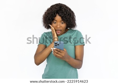 Shocked young woman reading news on phone. Astonished African American girl opening mouth and making big eyes, seeing unbelievable news. Studio shoot, emotion, technology concept