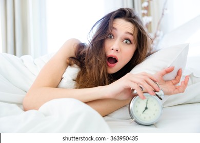 Shocked young woman waking up with alarm 