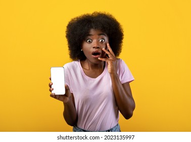 Shocking Mobile News Concept. Emotional Black Lady Showing Smartphone With Blank Screen To Camera Advertising New Amazing Application Over Yellow Background. Mockup