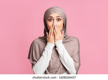Shocking news. Amazed arabic woman in headscarf covering her mouth with hands over pink background with free space