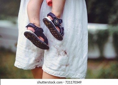 Shod Feet Of A Child In The Arms Of A Mother, A White Dress, Stained With Shoes, Raising Children And Loving Them