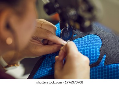 Shoe Factory Worker Making Black And Blue Sneakers Using Industrial Sewing Machine, Hands Holding Shoe Detail In Close Up. Footwear Manufacturing Industry Concept