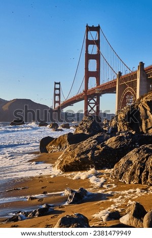 Shoe prints in sand coming from crashing waves at sunset with Golden Gate Bridge