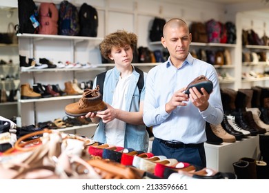 Shoe Salesman Helping Teen To Choose Fashionable Winter Boots At Shoe Store