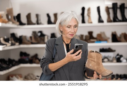 In shoe store, senior woman holds shoes in hands, takes sample of product out of window and scans QR code on shoe label. Using mobile application, visitor pays online. - Powered by Shutterstock