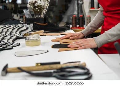 Shoemaker Is Adding Glue With A Brush To Some Pieces Of Leather That Will Be Used To Make Shoes. The Cobbler Is Working On His Desk In His Workshop.