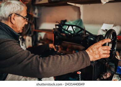 A shoemaker is sewing on a sewing machine at his cobbler's workshop. Profile of a senior cobbler using sewing machine at his manufacturing cobbler's workshop, repairing shoes and footwear. Craftsman. - Powered by Shutterstock