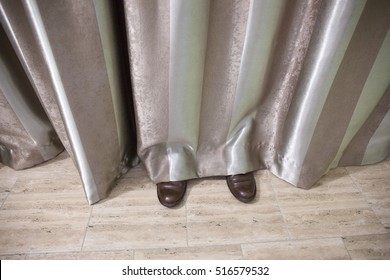 Shoes of a man hidden behind striped curtains in a room.  
