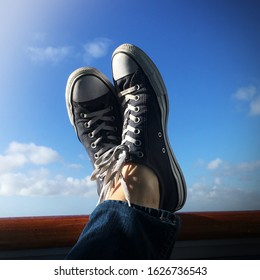 Shoes at sea - navy blue Chuck Tylor Converse All-Star sneakers propped up on the polished wooden rail of cruise ship, framed by a deep blue, sunny Caribbean sky.